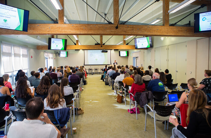 Conference room with people listening while seated in chairs during a sustainability presentation