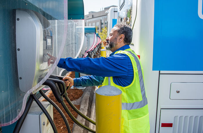 Man in a safety vest examining power cables at an electric vehicle charging station