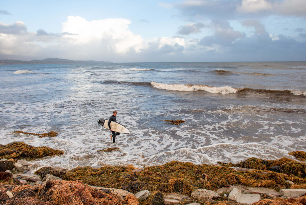 Male walking on Santa Barbara Beach in wet Suit and Holding Surf Board