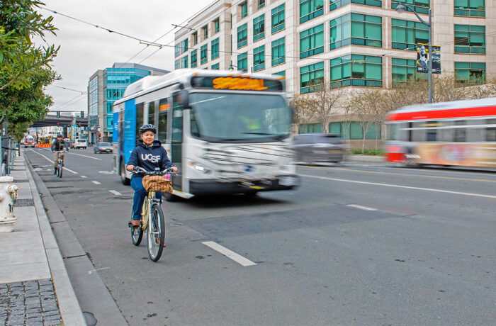 UCSF employee biking alongside a zero-emissions shuttle bus