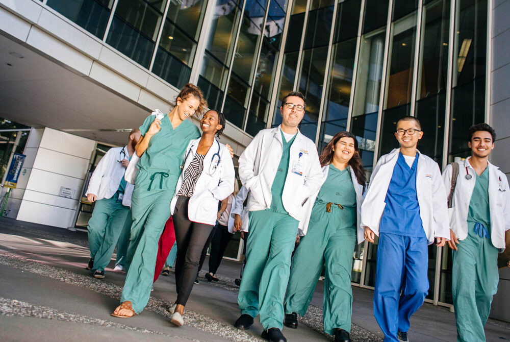 Group of male and female doctors in scrubs, walking out of hospital