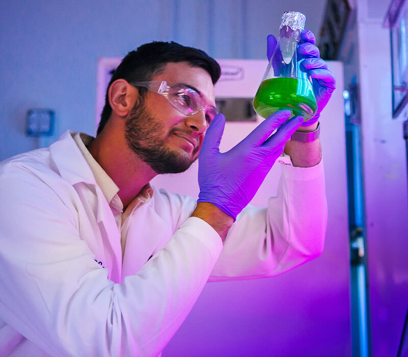 Student in lab clothes holding up and examining chemicals in a beaker