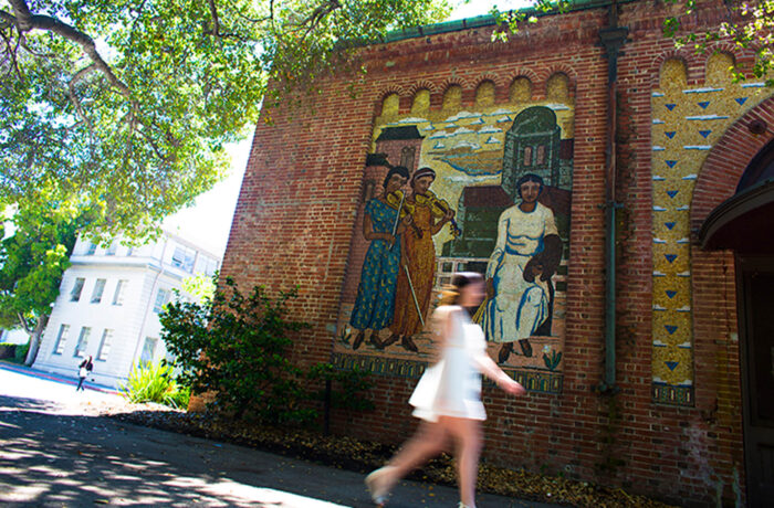 Woman walking in front of a mosaic on the side of a brick building