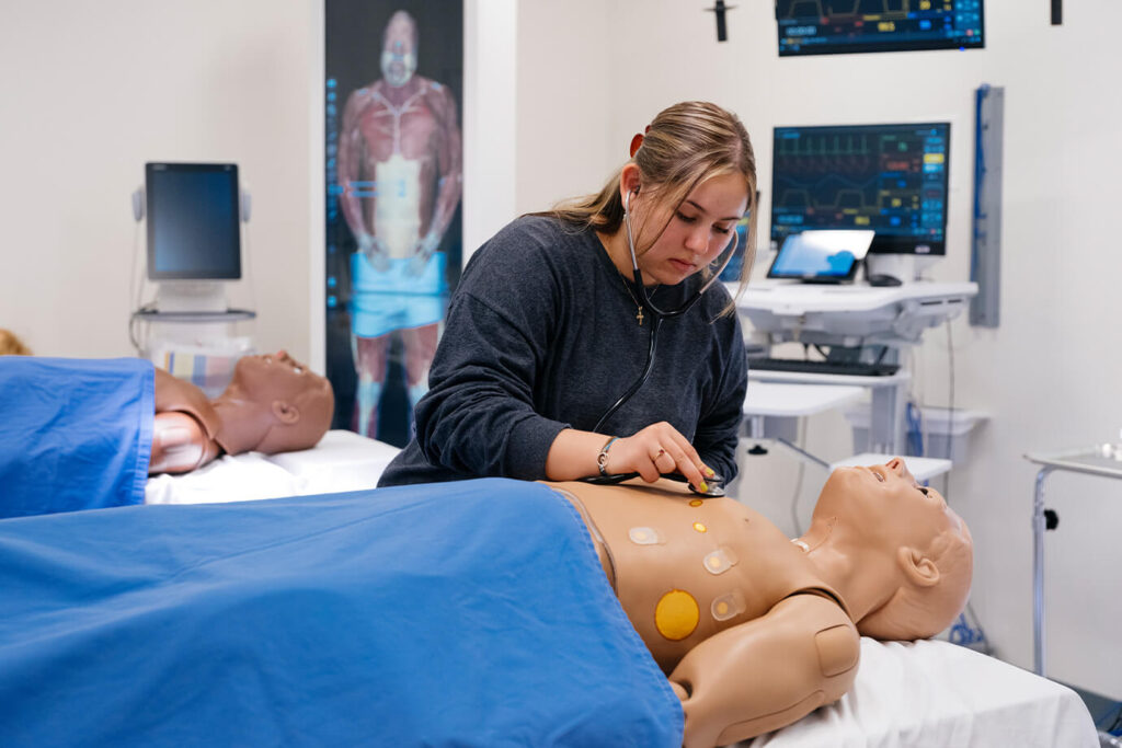 A medical student uses a stethoscope on a training manikin.