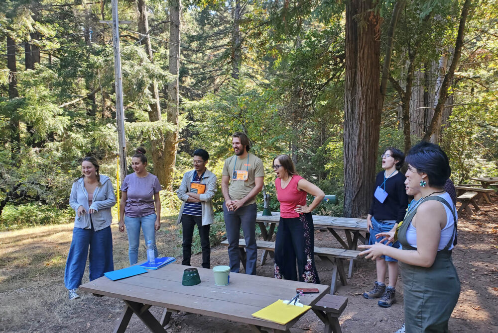 Students standing around picnic table in woods laughing