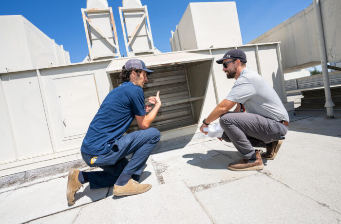Nico Fauchier-Magnan and Sam Cole from the Energy Engingeering team check airflow from a bypass damper on top of Ghausi Hall, one of their team's commissioning projects to increase energy efficiency