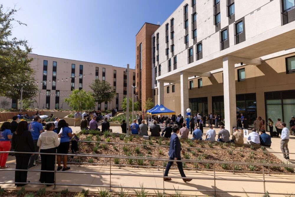 People standing and sitting in the courtyard in front of a campus building.